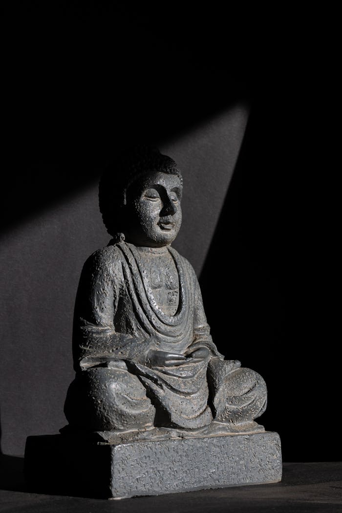 Sculpture of Buddha meditating in dramatic lighting, highlighting serenity and introspection.